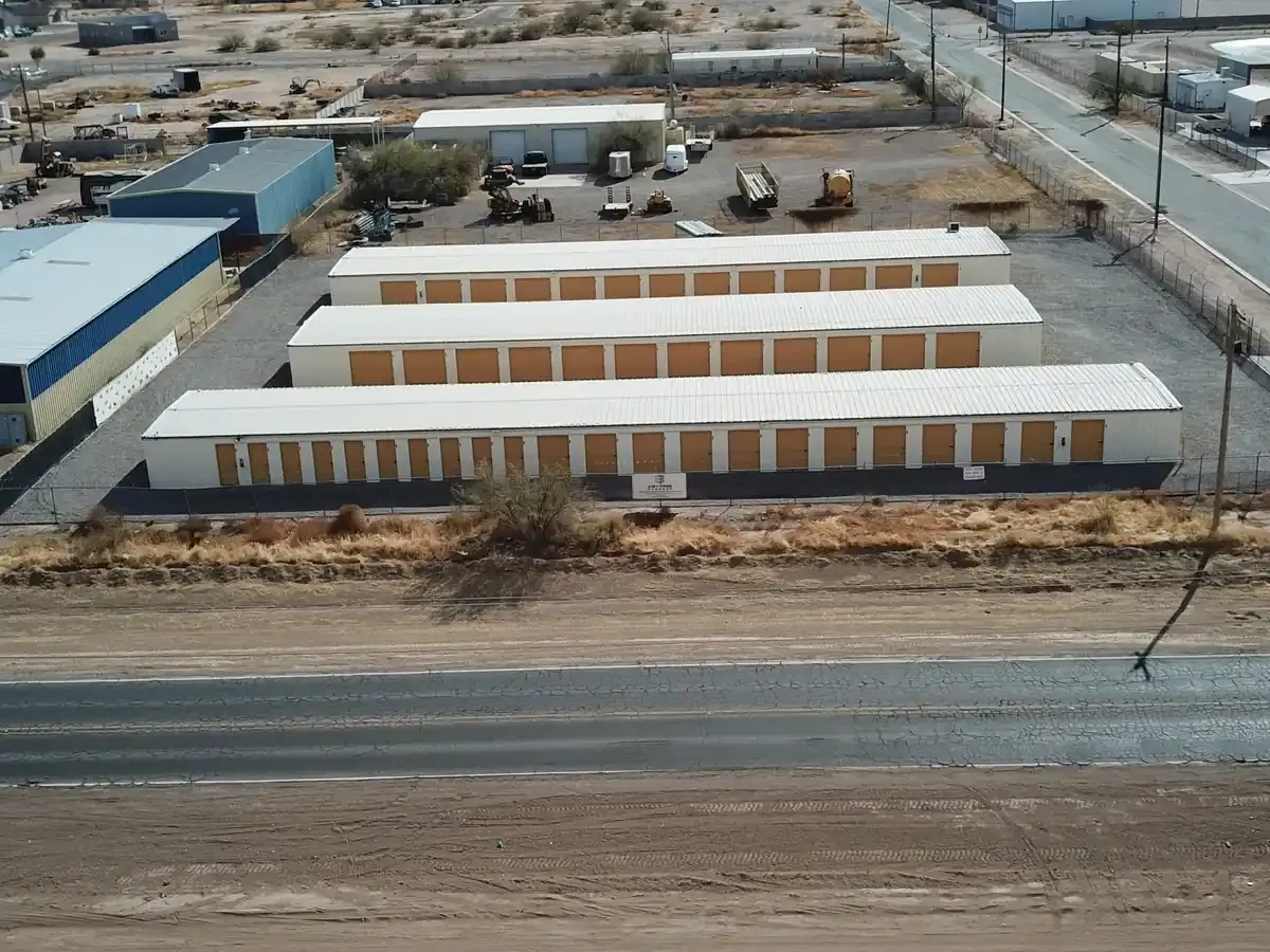Front-facing drone view of a self-storage facility showing three parallel rows of outdoor storage units with roll-up doors